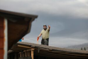 Homeowner photographs roof and ceiling damage while organizing insurance documents on a kitchen table.