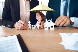 A family reviews insurance documents beside a car and laptop at a kitchen table.